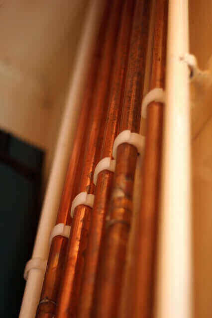 Wand mit offen verlegten Kupferohren.