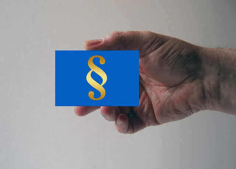 Foto einer Hand die von rechts eine blaue Karte in der Größe einer Visitenkarte mit den §-Zeichen in goldener Farbe ins Bild hält.
