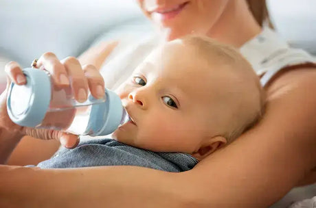 Baby liegt im Arm einer Frau und bekommt eine Flasche mit Wasser